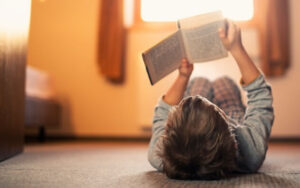 Little boy lying on the floor and reading a book. The boy is aged 6. Sunny day.
